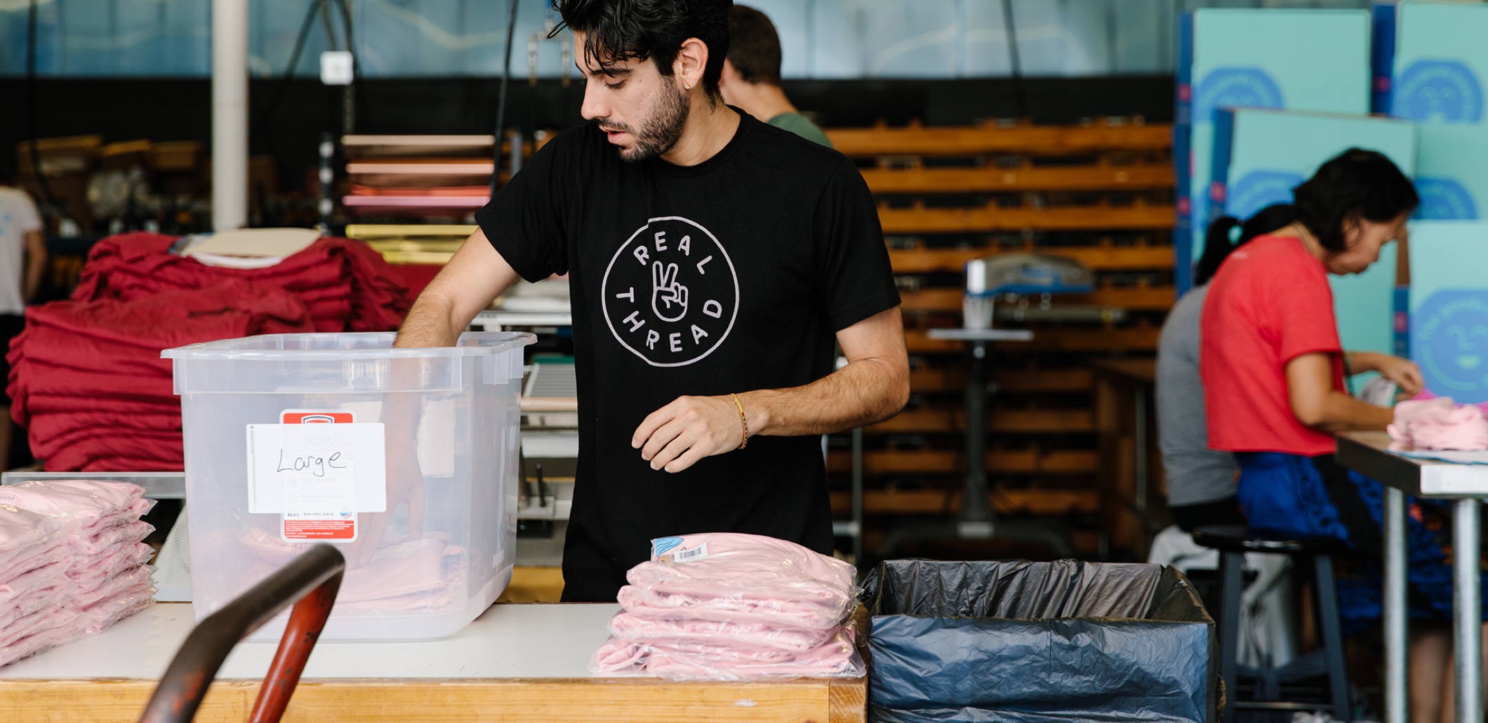 A man starts packaging an order of custom t-shirts. 