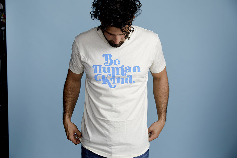 man pulling down white shirt in front of blue backdrop 
