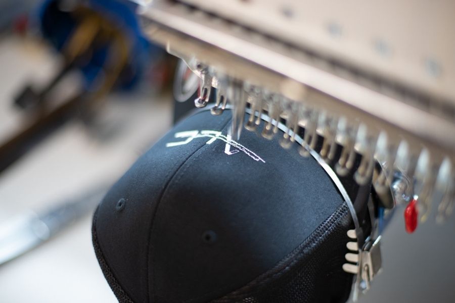 The needle punctures the hat to embroider it