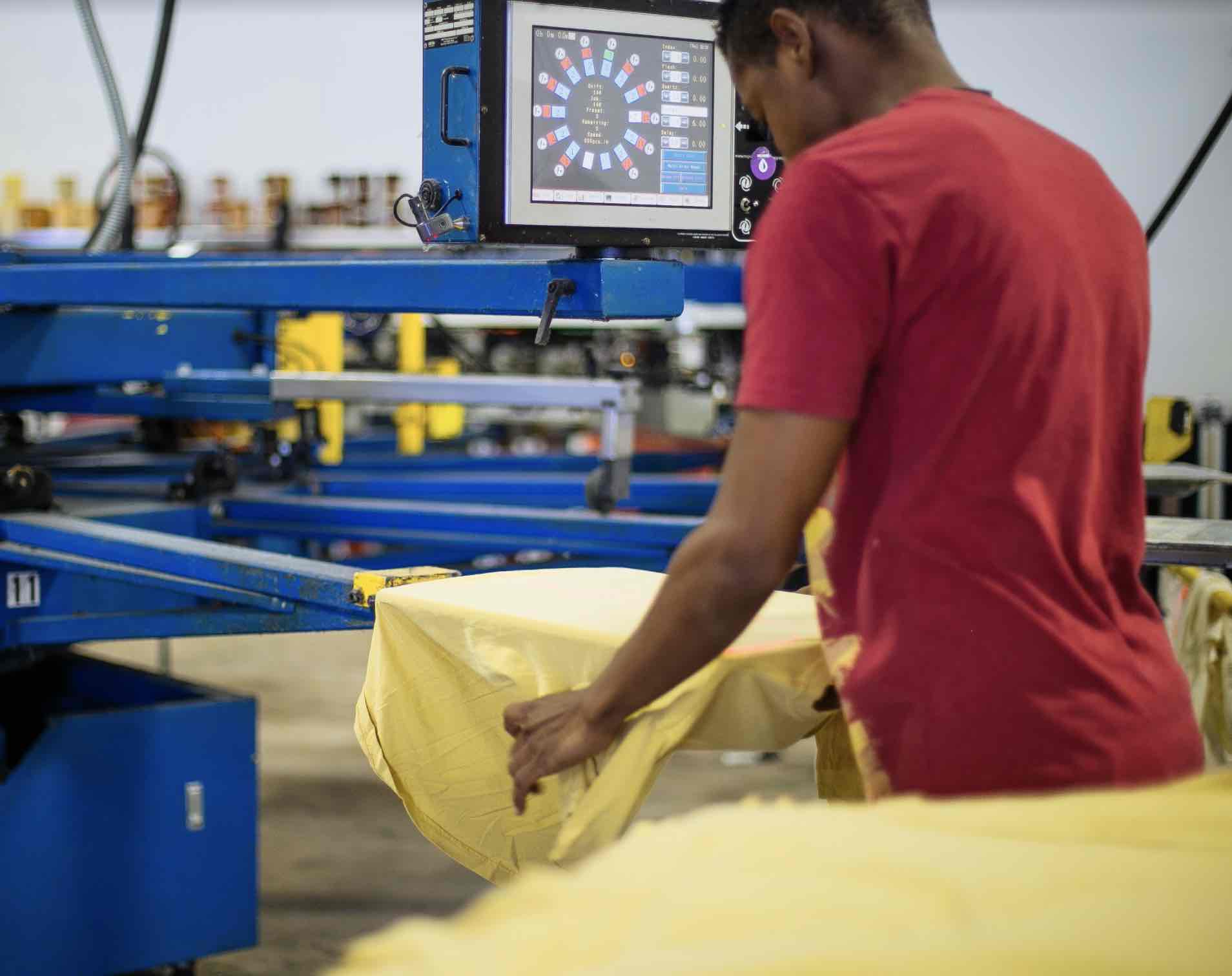 A man loads shirts onto a printing press.