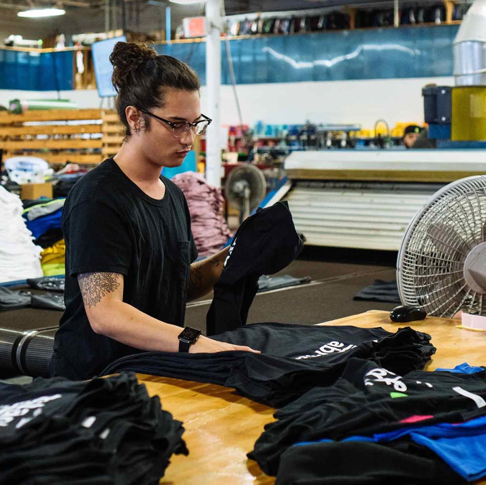 A man folds shirts that have just been printed, checking to make sure they are up to standards