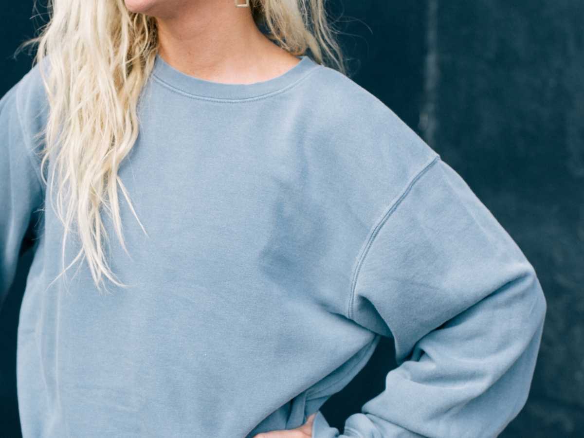A blonde-haired girl wears a steel blue pullover sweatshirt.