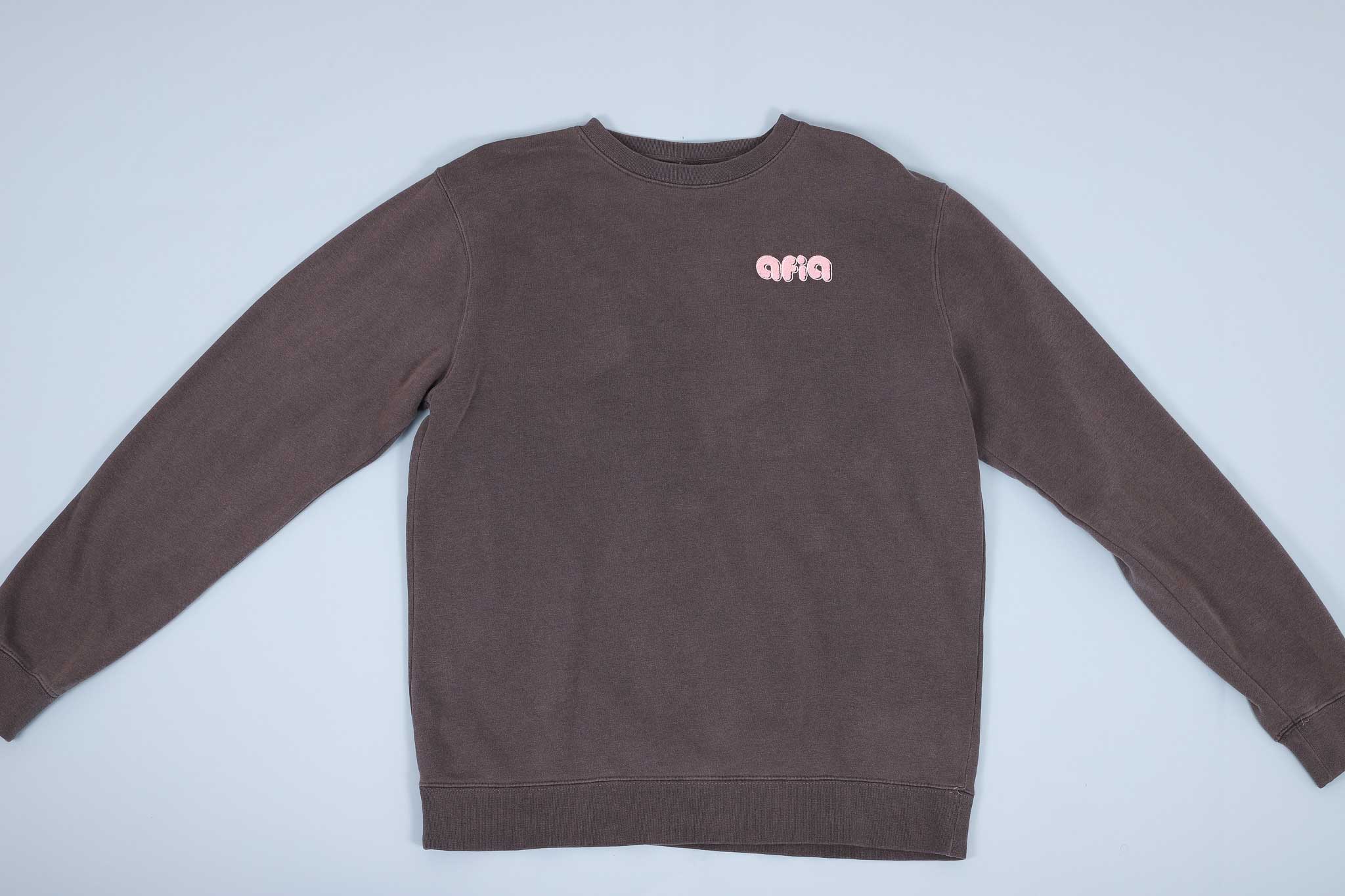 Grey sweater with pink text on the chest spread out on a light blue background