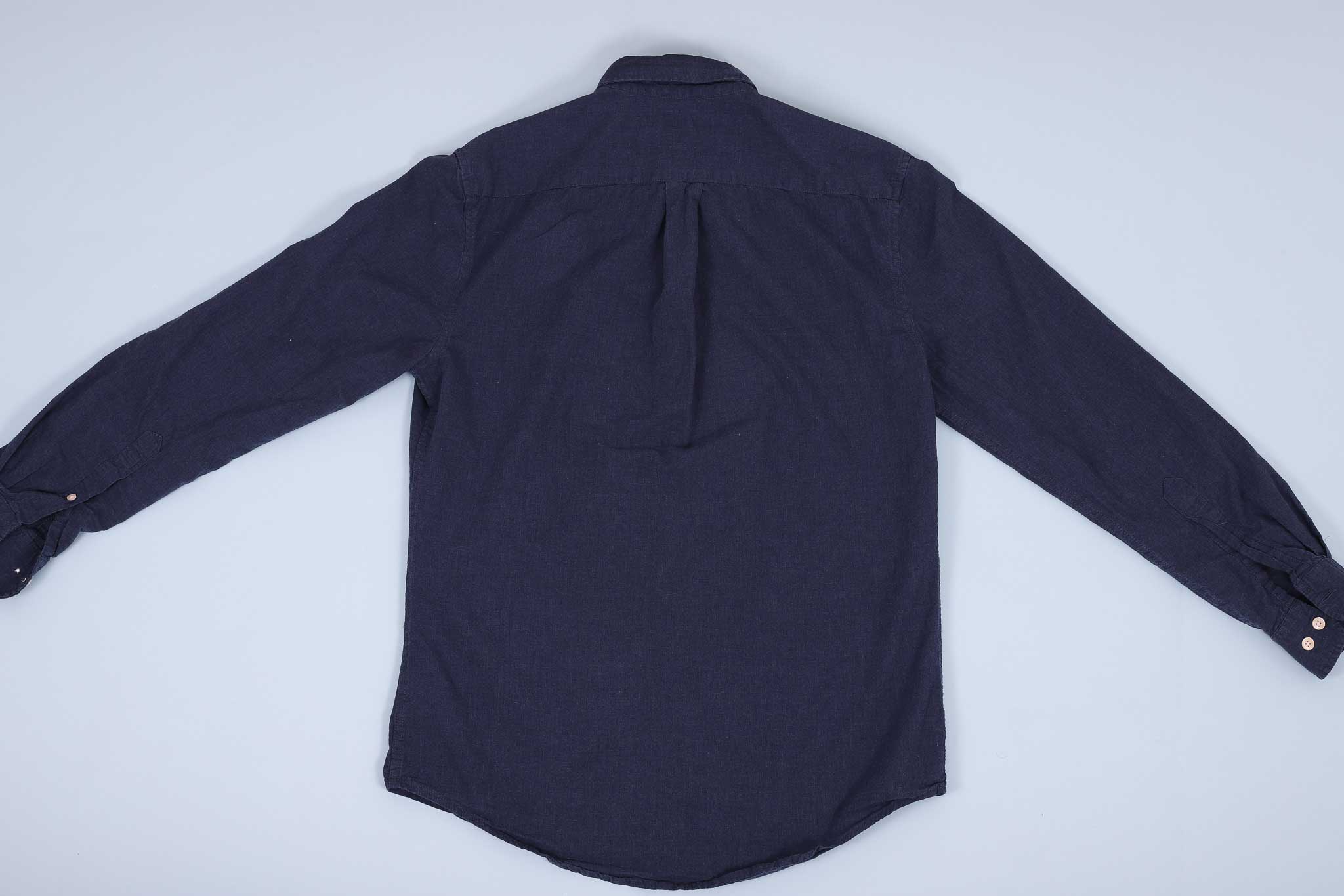 Navy buttoned up shirt spread out facing down against a light blue background