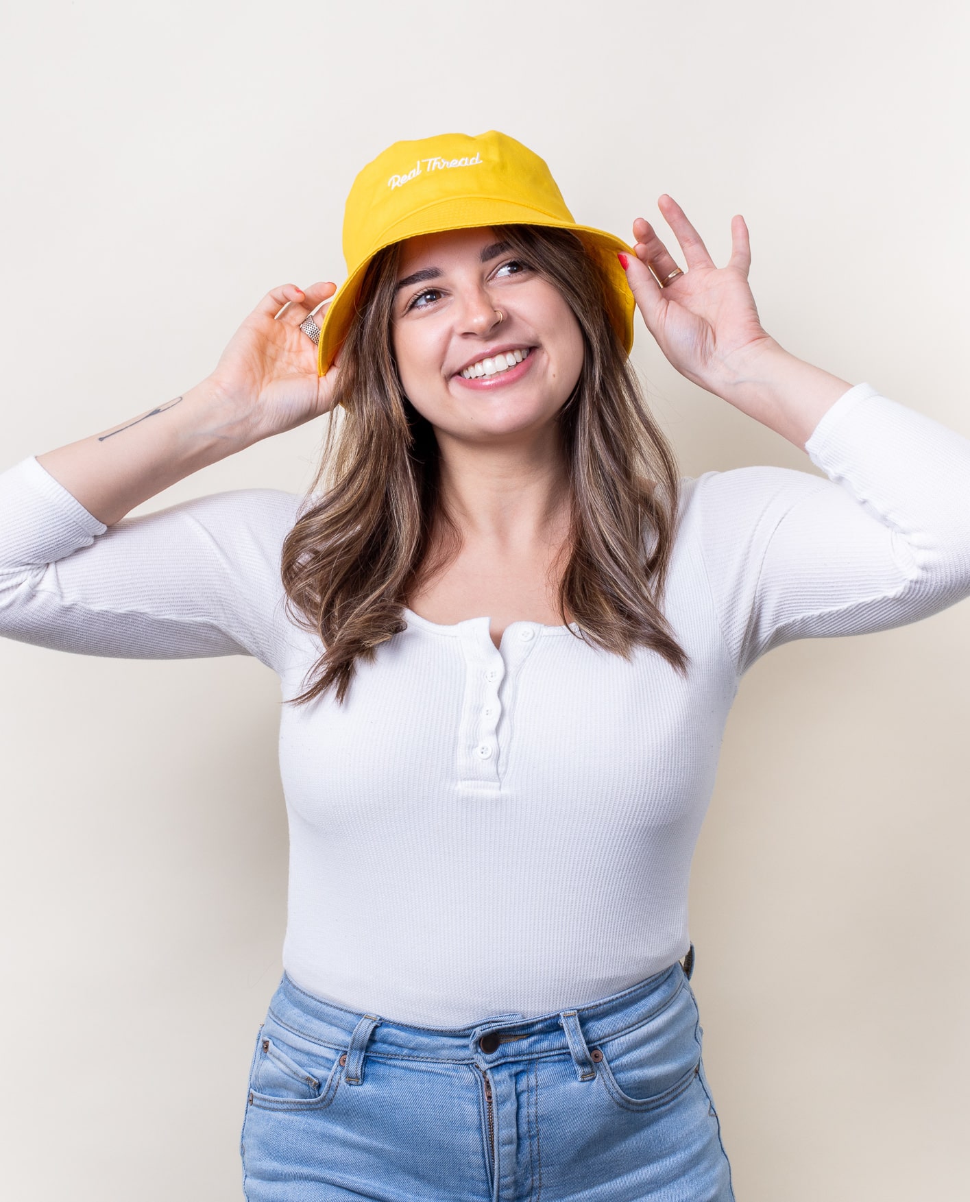Woman smiles wearing a yellow bucket hat with white embroidery