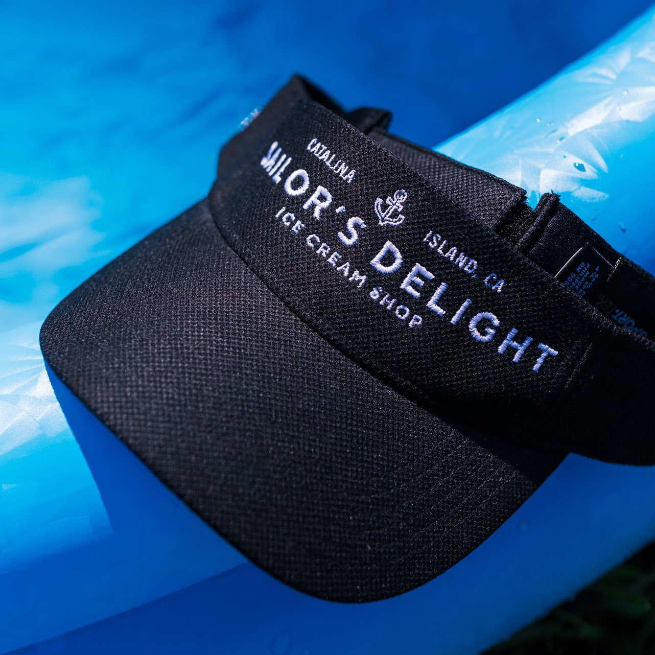 A black visor hat with white embroidery sits on the edge of a pool